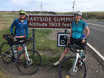 Jane standing beside her bike next to a road sign reading Hartside Summit